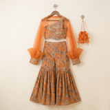 Rust Orange Paisley Printed One-Shoulder Sharara Set with Organza Cape Sleeves and Matching Potli Bag.