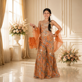 Rust Orange Paisley Printed One-Shoulder Sharara Set with Organza Cape Sleeves and Matching Potli Bag.